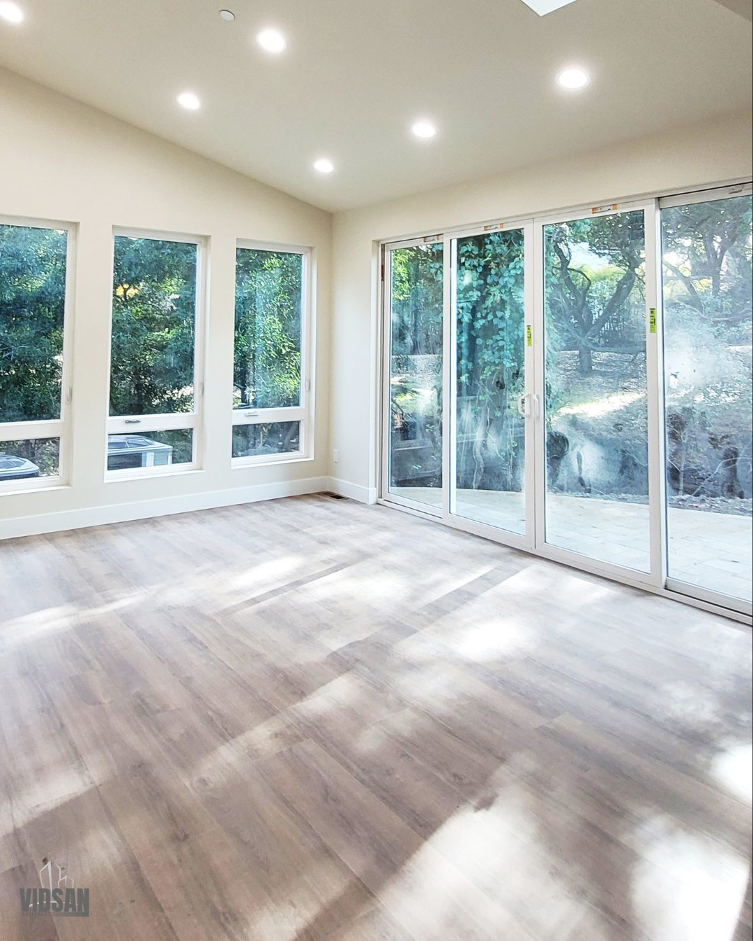 Sunlit room addition with wide-plank flooring and a full wall of sliding glass doors opening to a wooded backyard.