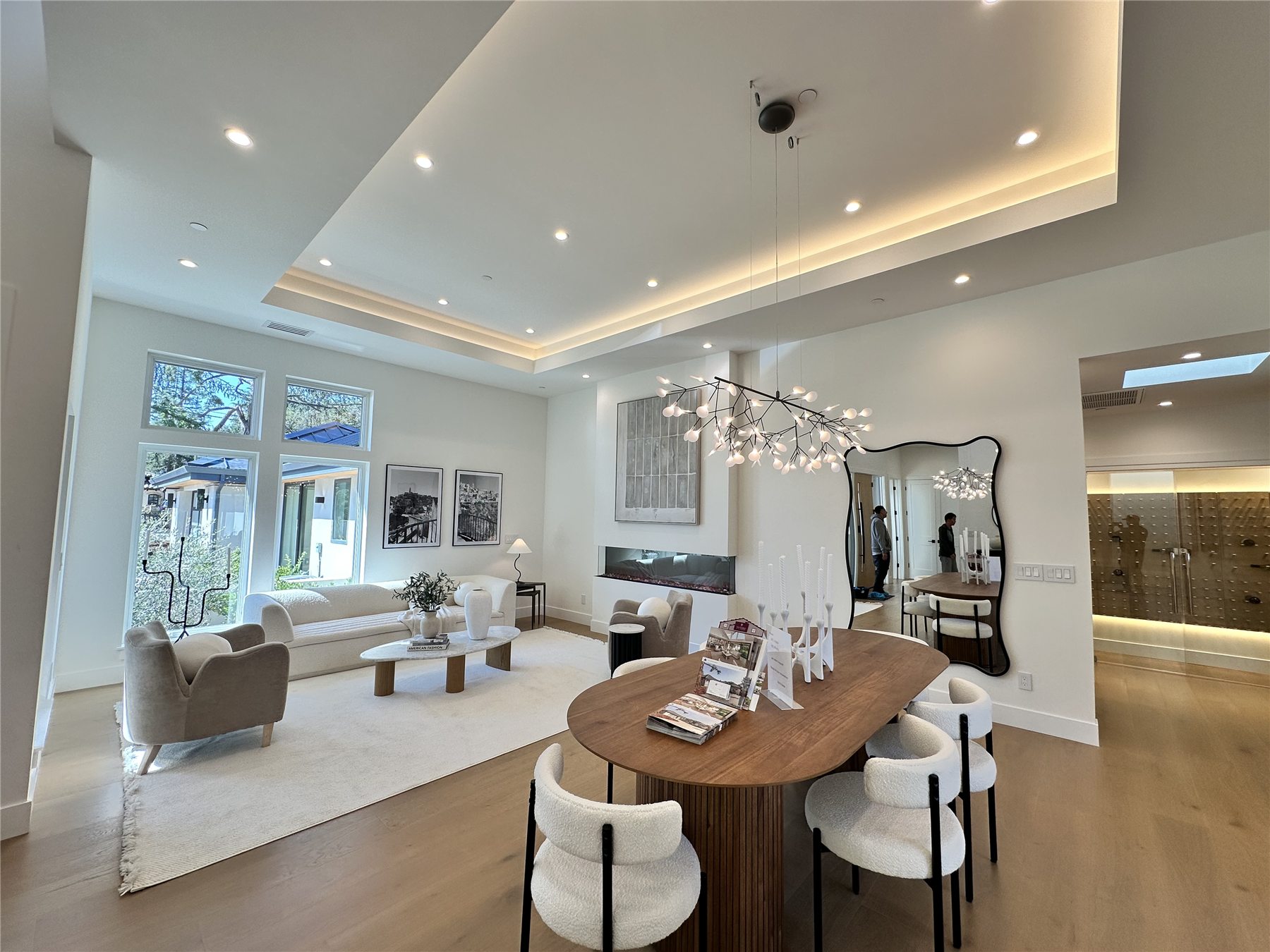 Living and dining area with a sculptural branching chandelier, gas fireplace, and a curved black console.