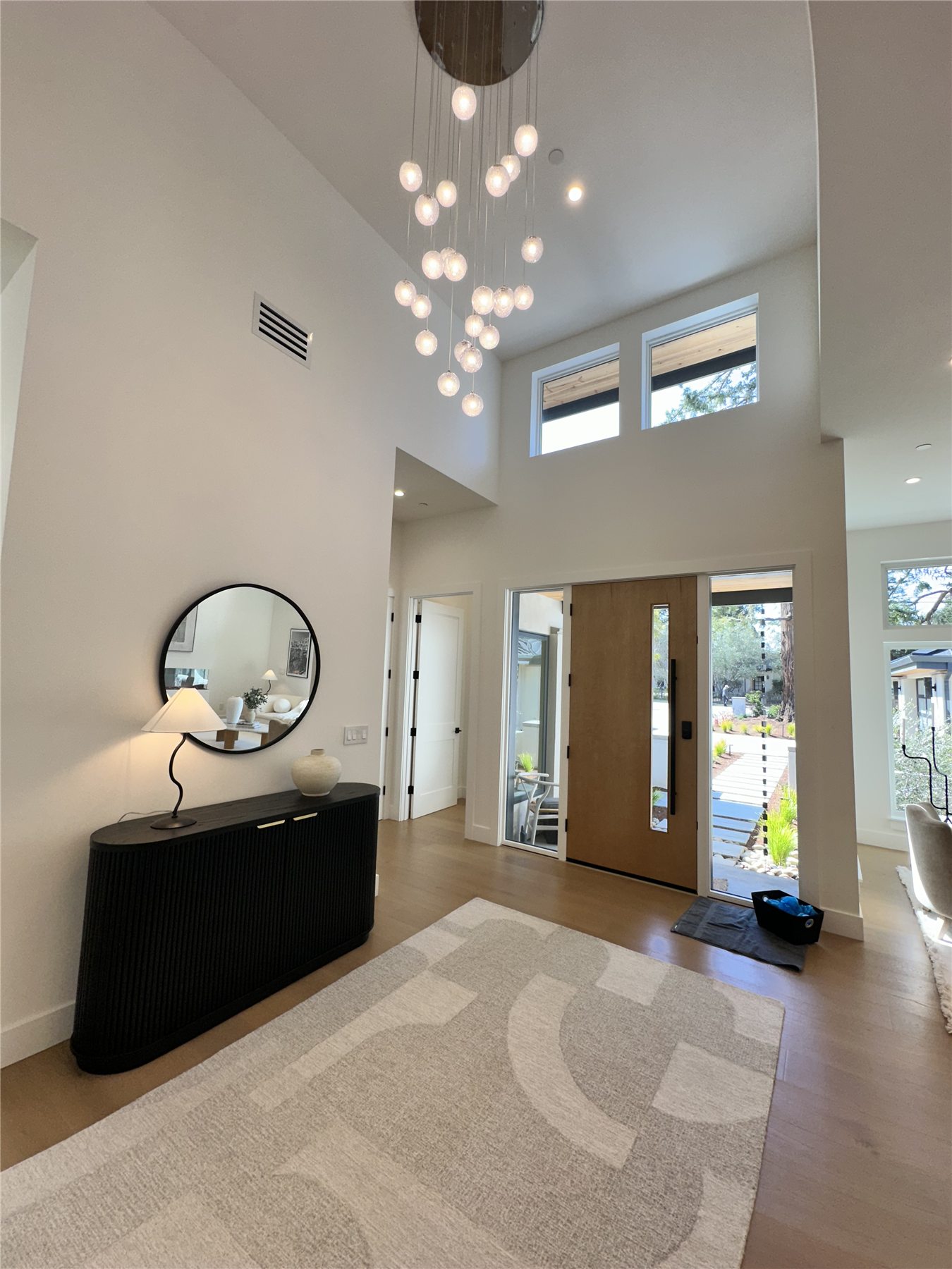 Entry foyer with a cascading glass-orb chandelier and a round mirror above a black console table.