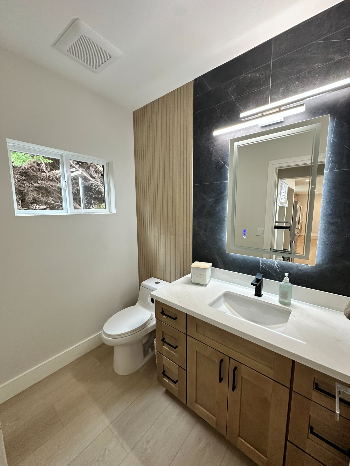A bathroom finished in dark stone, with a backlit mirror and a glass-enclosed shower.