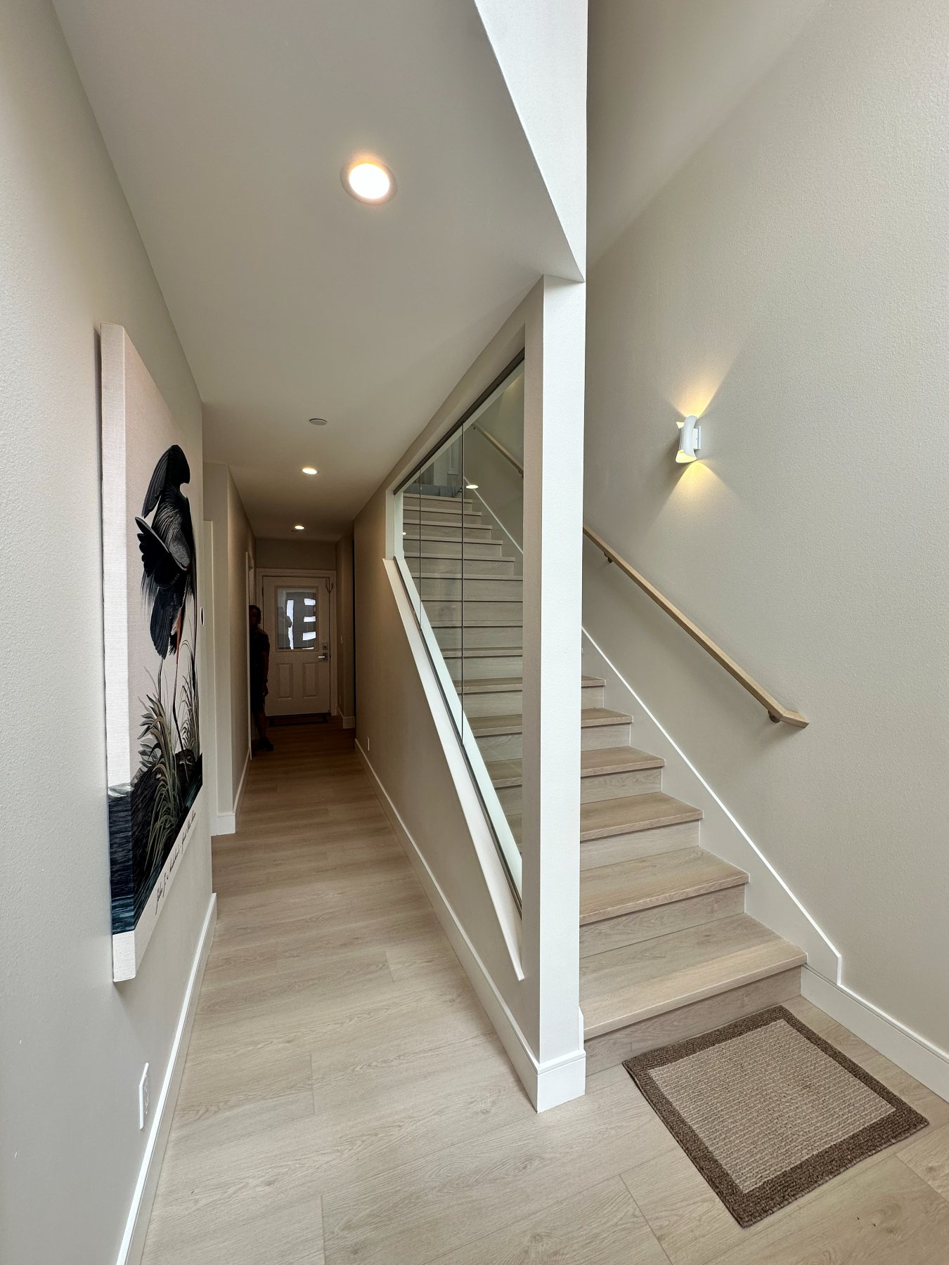 A hallway landing with a glass stair railing leading down to the entry.