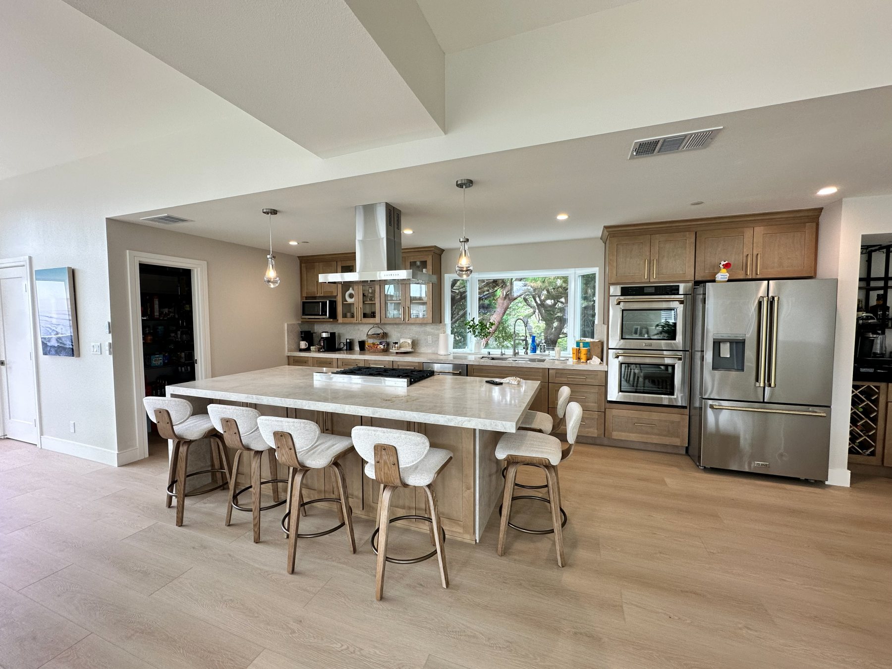 Kitchen island with bar seating for six, finished in wood cabinetry beneath a bay window.