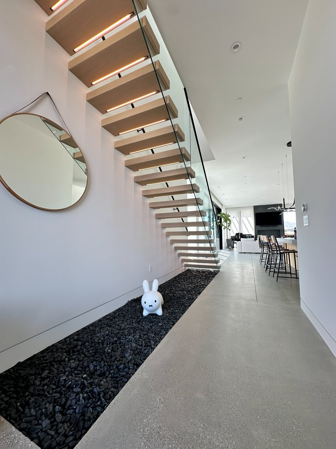 A floating wood staircase with a glass railing, set above a river-rock accent bed.