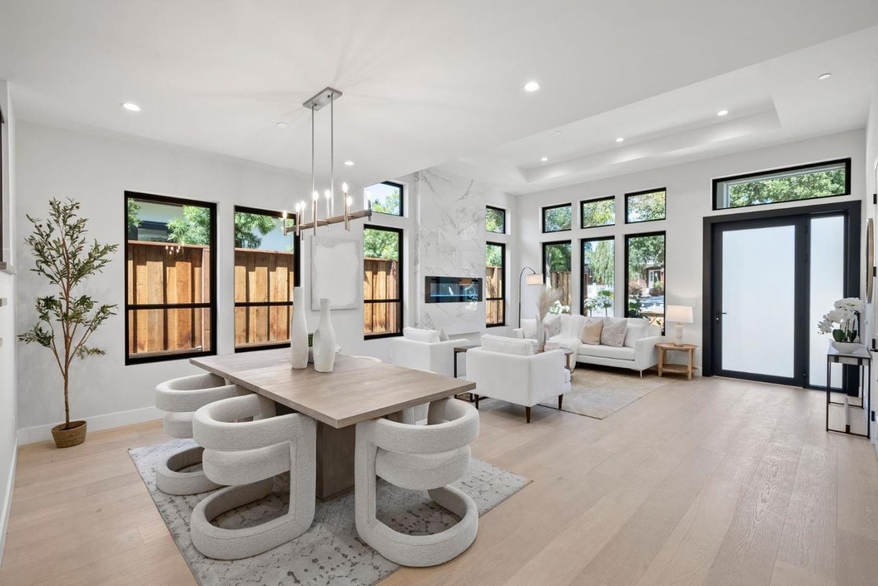 Living and dining space with a marble fireplace surround, black steel-framed windows, and a sculptural dining table.