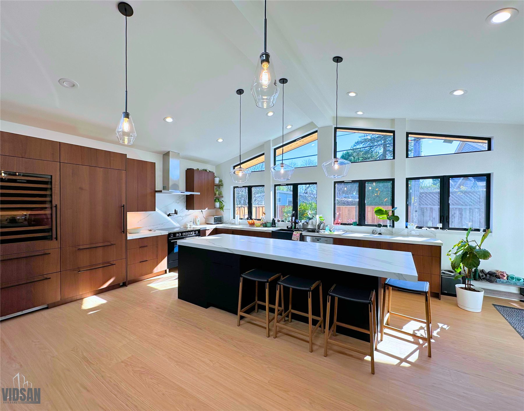 Kitchen with a long waterfall-edge island, walnut cabinetry, and a run of clerestory windows under a vaulted ceiling.