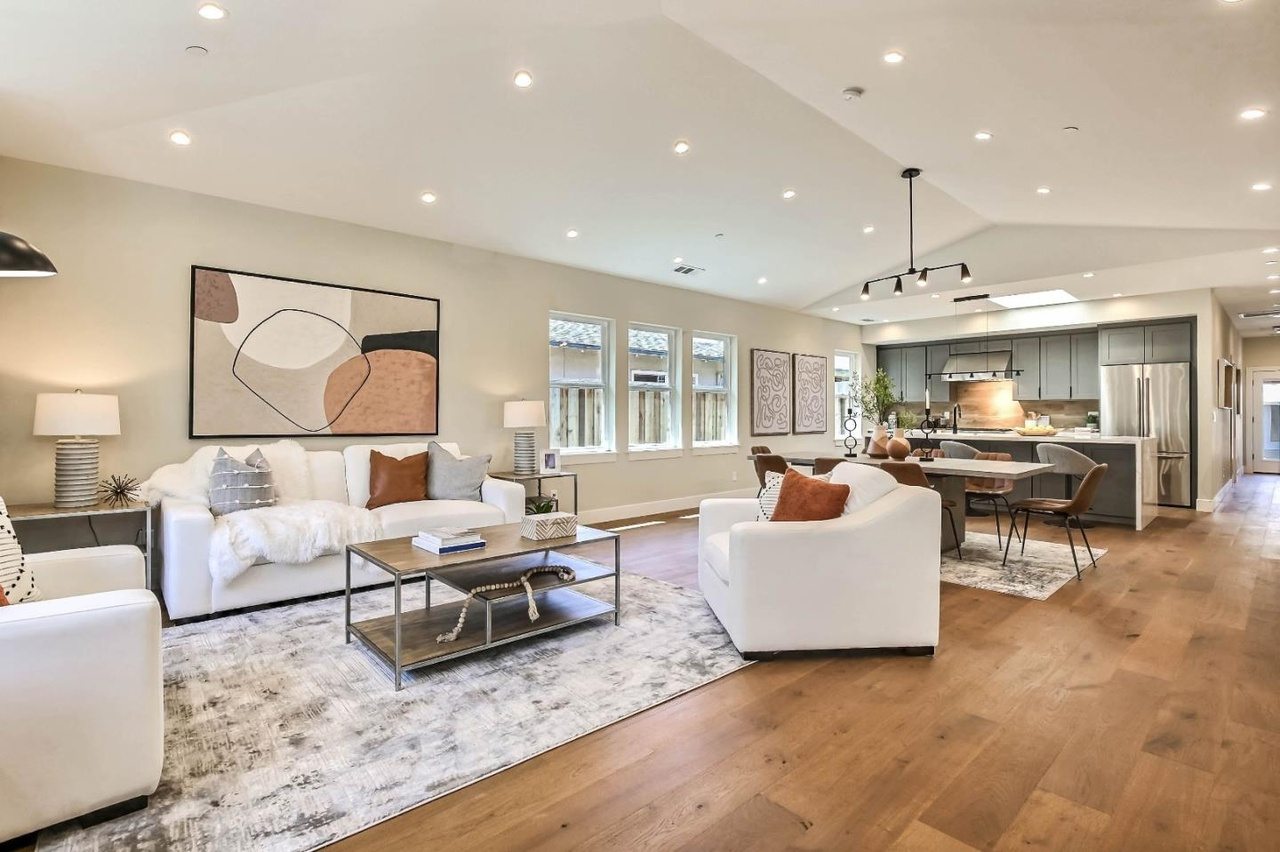 Open-concept great room with white seating and wide-plank oak floors, opening to the kitchen beyond.